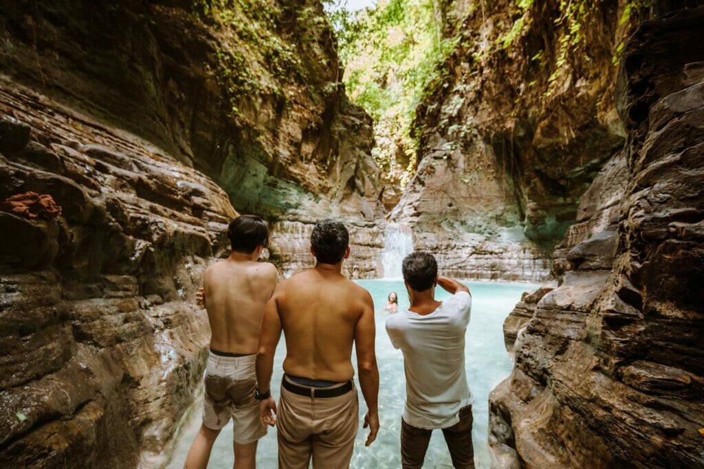 men-standing-with-back-to-camera-at-waterfall-in-sumba-indonesia